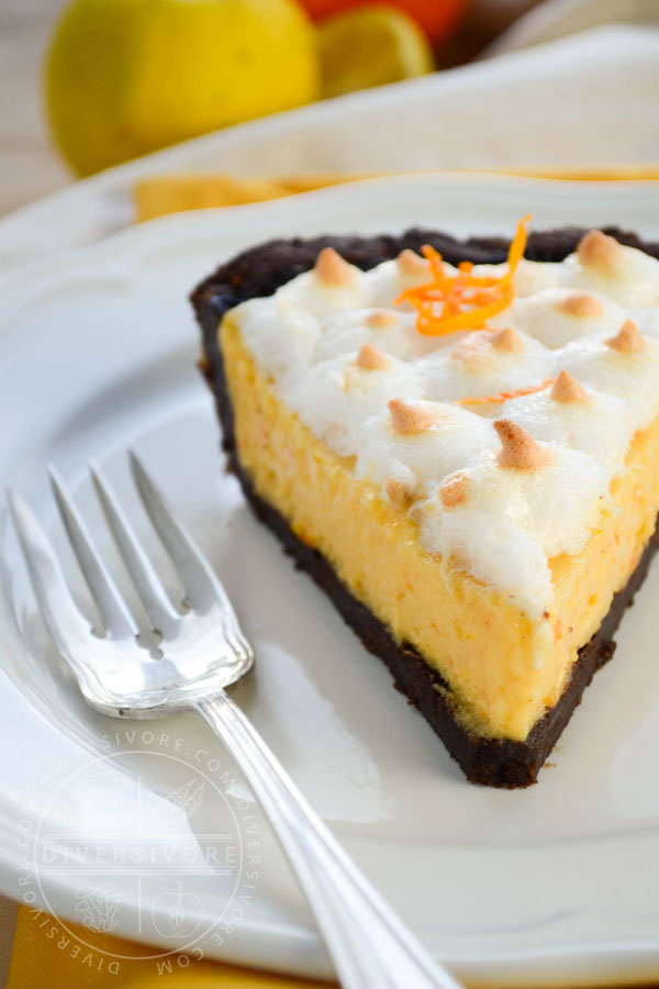 A slice of seville orange pie with meringue and a chocolate graham wafer crust, served on a white plate with a silver dessert fork