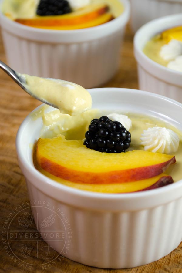 Peach pots de creme with peach slices and a blackberry in a white ramekin, with a small spoon removing a portion