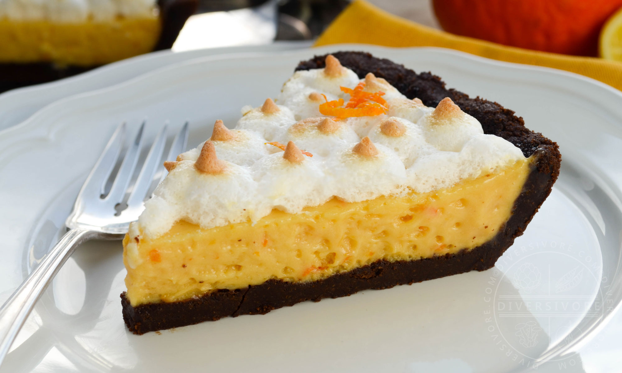 A slice of seville orange pie with meringue and a chocolate graham wafer crust, served on a white plate with a silver dessert fork