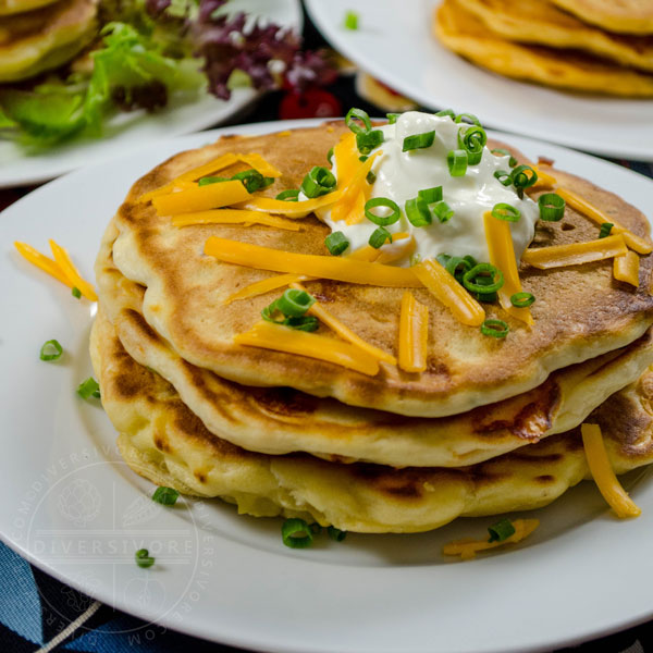 Bacon, cheddar, and chive pancakes topped with sour cream, cheese, and chives, all served on a white plate